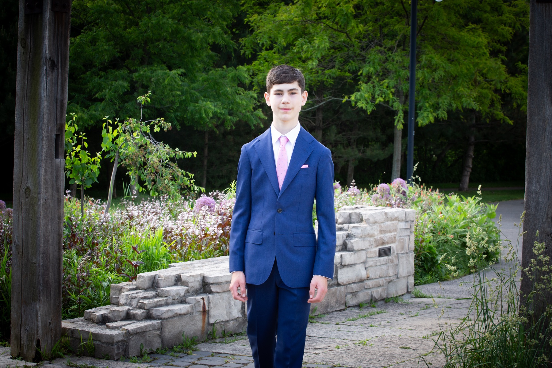 Evan Uster in a navy suit, standing beneath a garden pergola